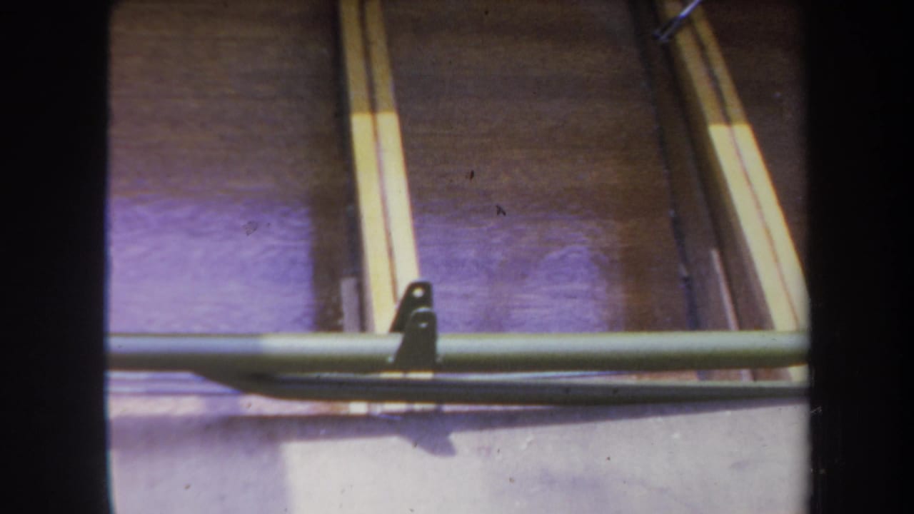 Wooden boat interior with green metal support bar, brackets, and sunlit planks.