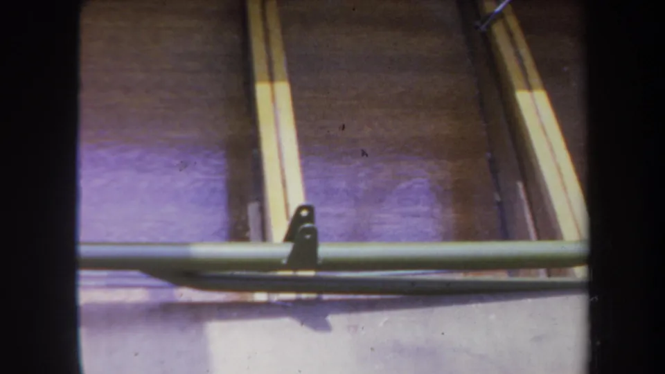 1969 Yucaipa frame of a wooden boat interior, with a green cross support, brackets, pale strips, and purple-toned shadow.