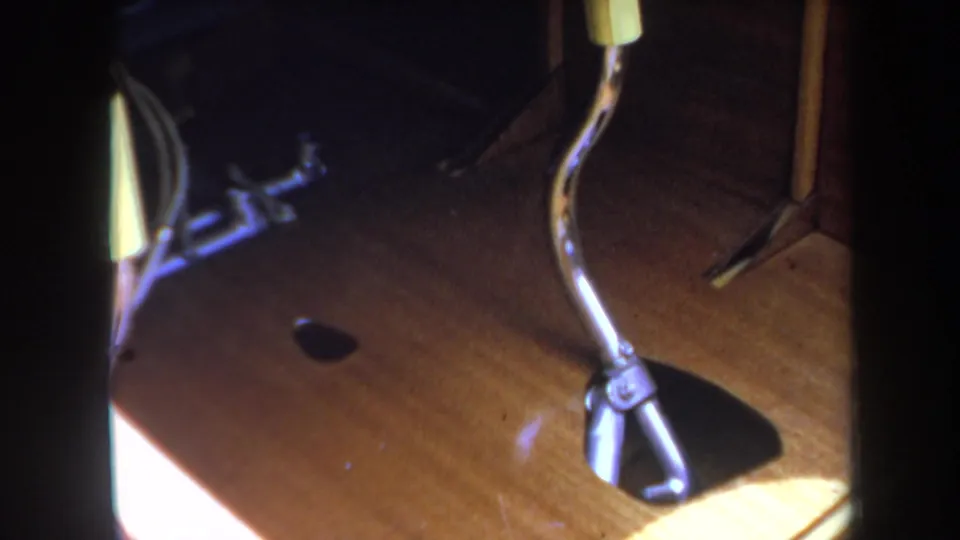 Close 1969 home-movie view of model airplane landing gear, curved struts, and a wheel assembly against a warm wooden surface.