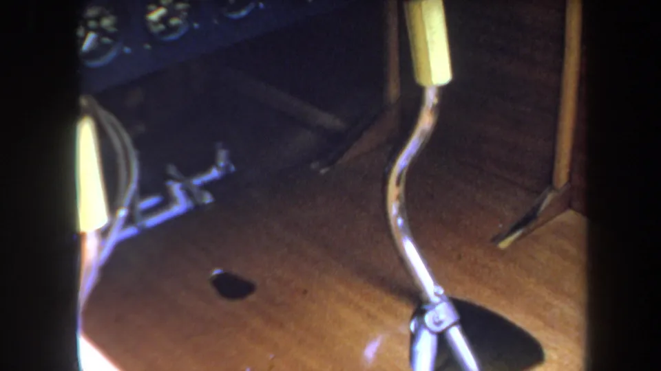 1969 8mm frame showing an angled tabletop view of model airplane landing gear, a small wheel, metal hardware, and wood grain.