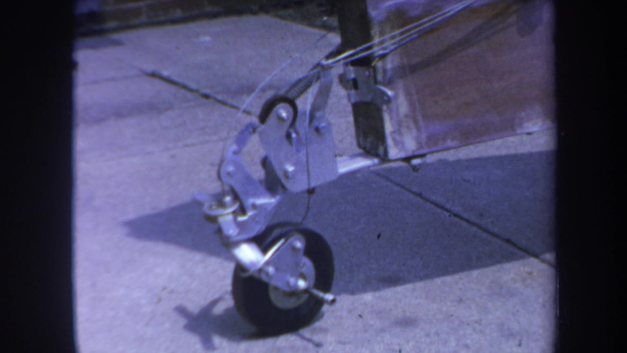 Small wheel assembly and metal hardware beside a wooden beam on a paved surface.