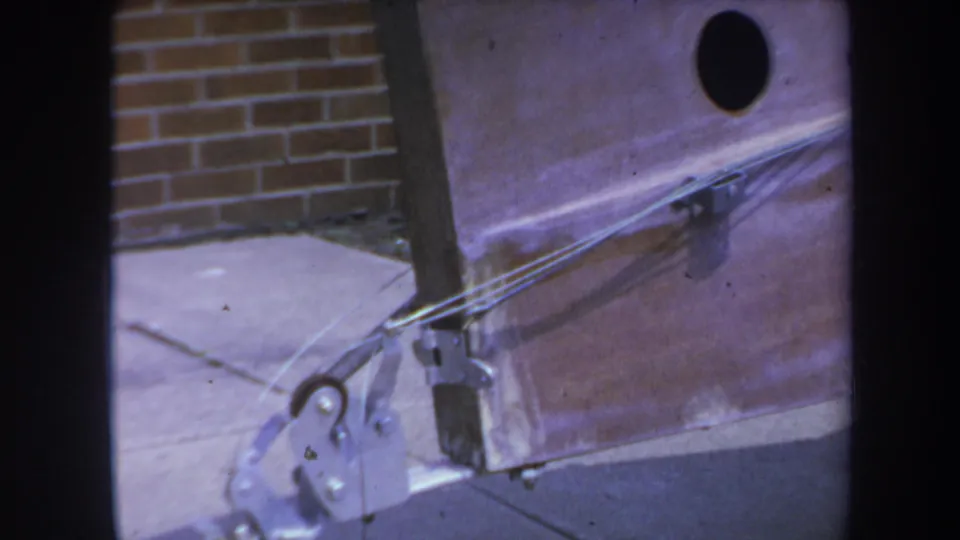 Close 8mm view of the trolley mechanism in California metadata, with bracket plates, taut wires, sidewalk, and brickwork visible.