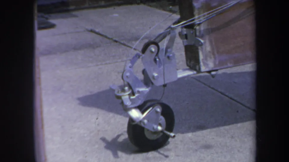 1969 Yucaipa 8mm frame showing the front caster wheel and metal bracket of a homemade trailer on a driveway.