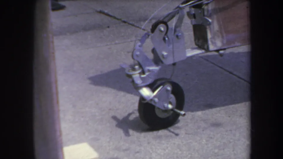 1969 Yucaipa 8mm frame with a homemade trailer's black caster wheel, metal hardware, and driveway surface in view.