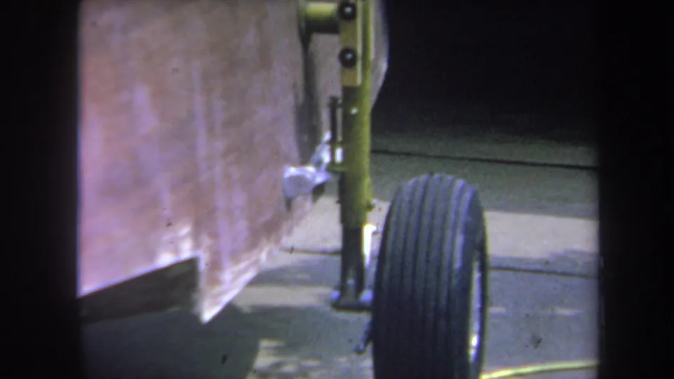Tight 1969 8mm frame of a home-built trailer's wheel and yellow-painted suspension or axle detail on a driveway in Yucaipa.