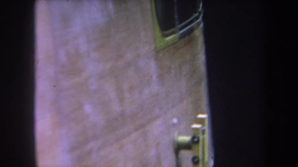Color-faded 8mm frame from Yucaipa showing the side of a handmade wooden structure with metal fasteners and a small window-like opening.