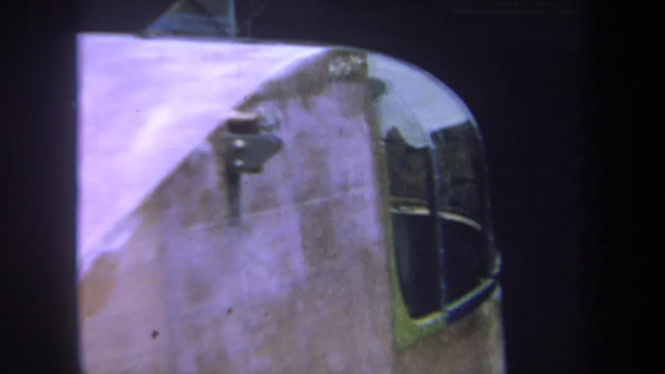 8mm home-movie frame showing a rounded section of the handmade wooden structure, dark inset panels, and small metal hardware.