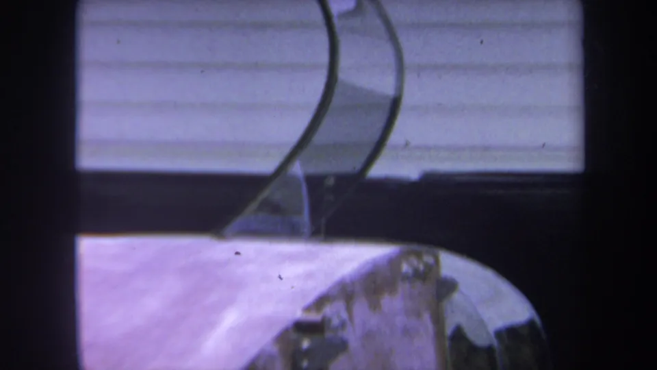 1969 Yucaipa 8mm frame showing curved metal supports, a wooden rounded section, and light horizontal siding behind the object.