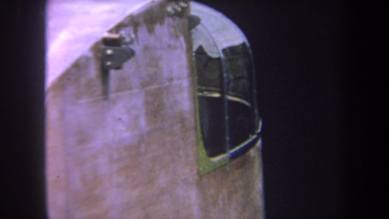 1969 8mm home-movie frame from Volmer Yucaipa showing a close aircraft cockpit window, riveted fuselage, and purple film cast.