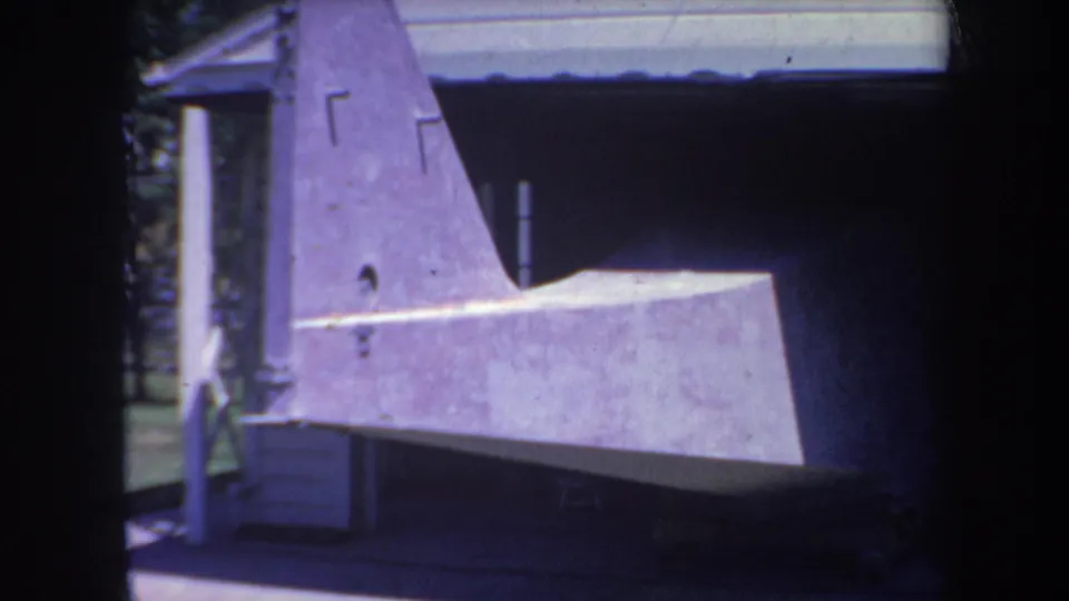 1969 Yucaipa-area 8mm frame showing a gray aircraft assembly in an outdoor shaded storage area.