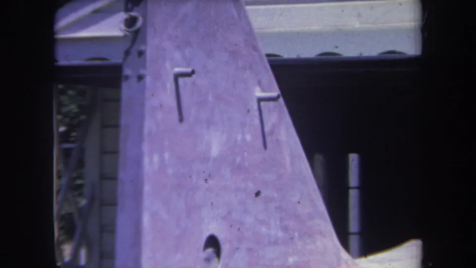 Close 1969 8mm view of the purple tail fin, rivets, and house exterior during an aircraft construction scene.