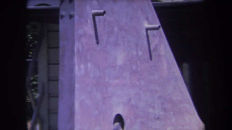 Close Yucaipa 1969 frame of an unfinished aircraft tail fin with hardware marks beside a garage opening.