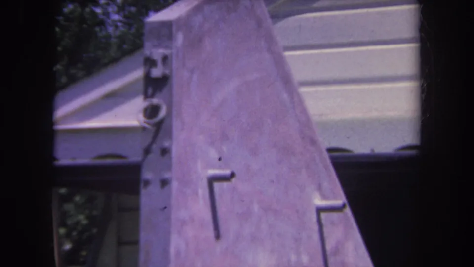1969 Yucaipa home-movie frame showing the sloped purple-tinted metal sculpture surface with background siding.