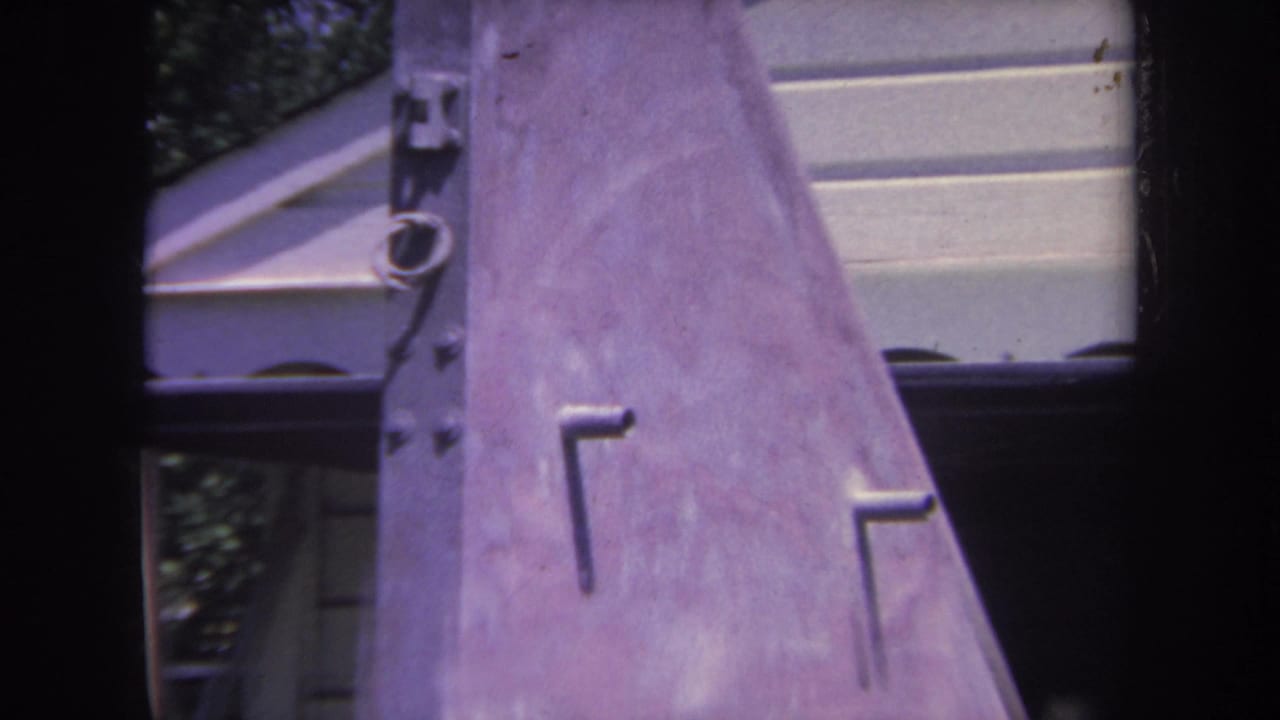 1969 8mm frame from Yucaipa showing a close, partial view of a metal airplane tail near a residential house and shaded trees.