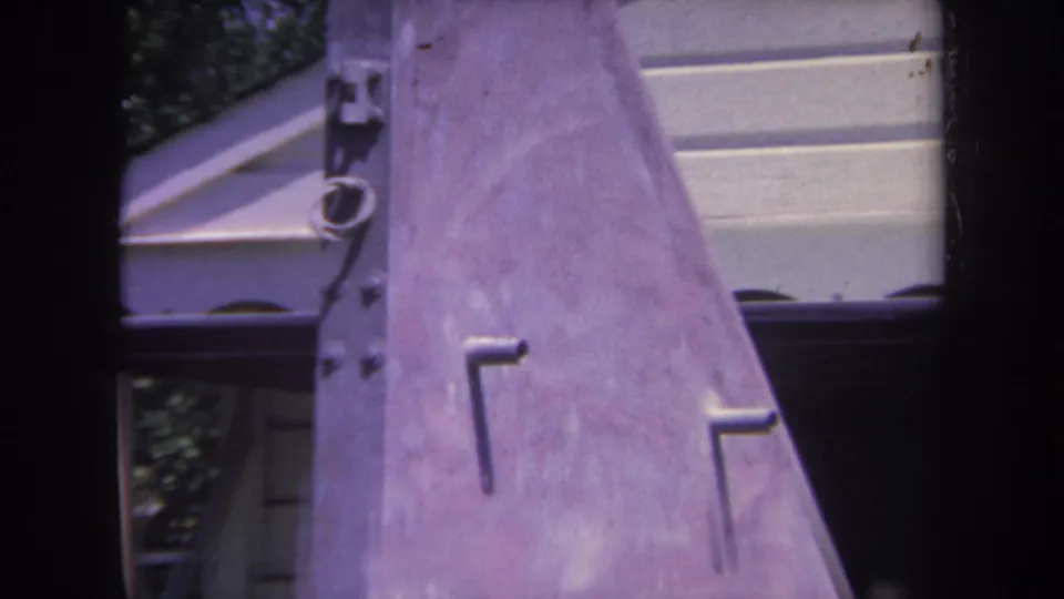 1969 8mm frame from Yucaipa showing a close, partial view of a metal airplane tail near a residential house and shaded trees.