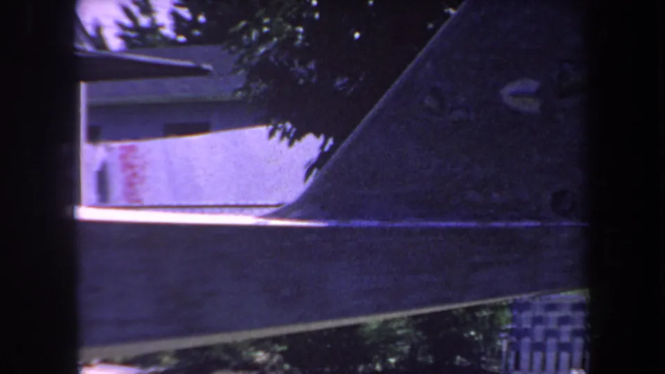 1969 home-movie frame showing a side section of the airplane tail and stabilizer against a shaded residential yard.