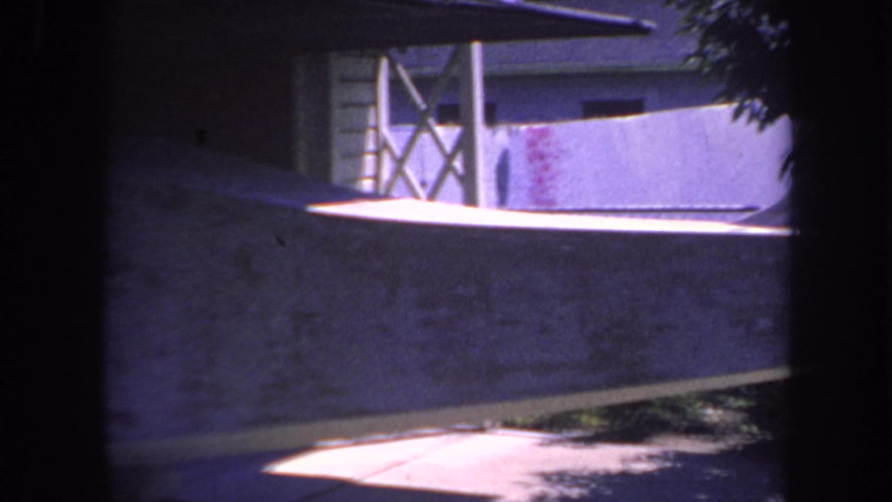 1969 Yucaipa-area 8mm frame looking from shadow toward a textured wall, wood siding, cross-bracing, and bright floor patch.
