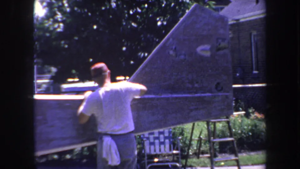 Man in a cap and white shirt works on a large aircraft tail section outdoors in Volmer Yucaipa, California, in 1969.