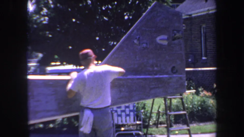 Rear view of a man cleaning or repairing a metal aircraft tail section in a 1969 Volmer Yucaipa home-movie frame.