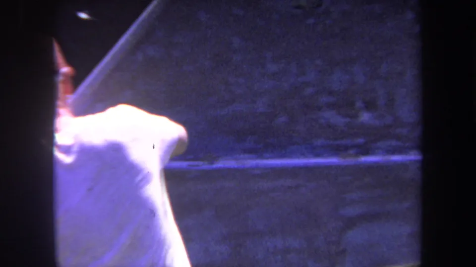 1969 Yucaipa home-movie frame showing a man from behind as he works with one arm raised near a large wooden surface.