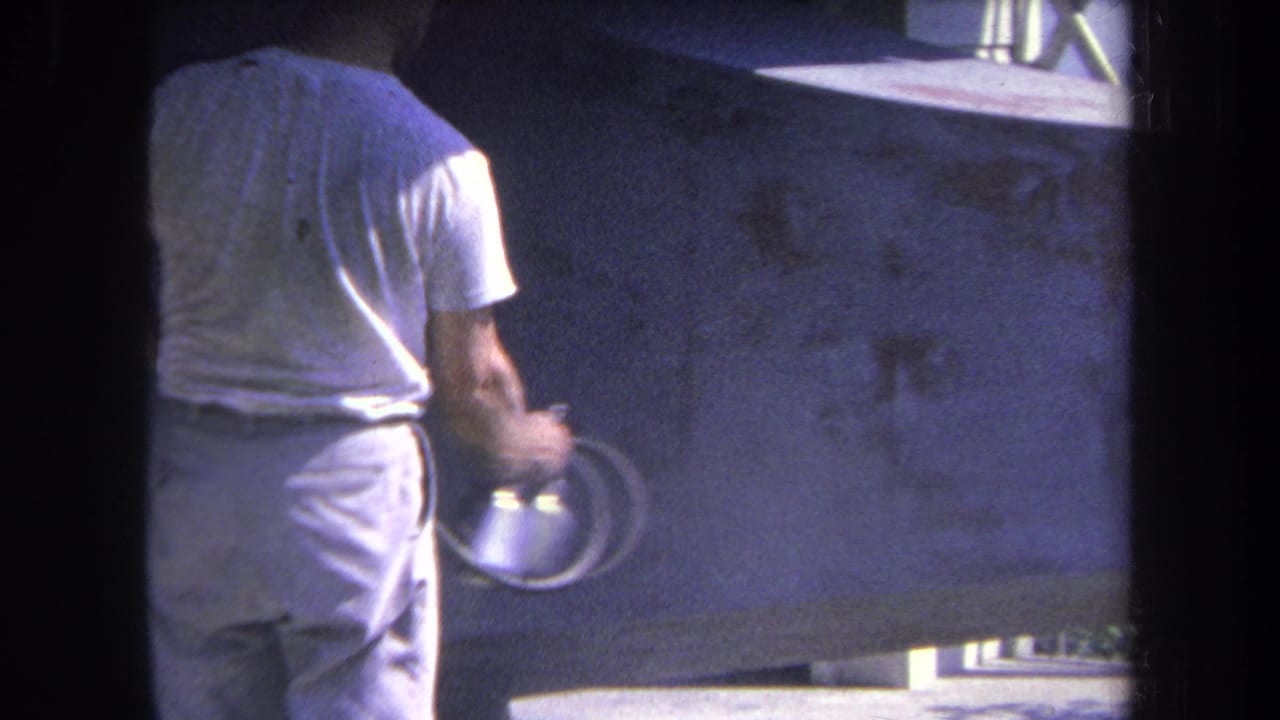 1969 Yucaipa-area 8mm frame showing a man from behind holding a spray gun near a large concrete wall.