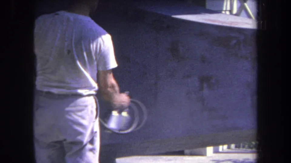1969 Yucaipa-area 8mm frame showing a man from behind holding a spray gun near a large concrete wall.
