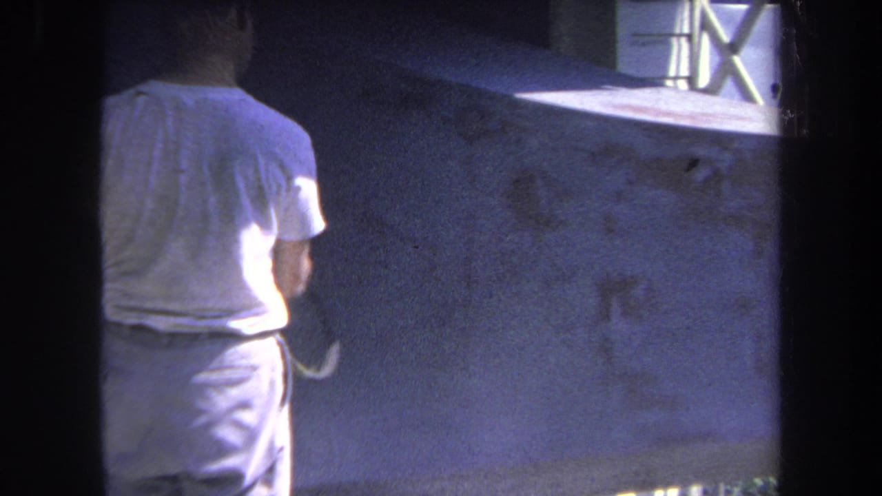 Man seen from behind aims a spray gun toward a concrete wall.