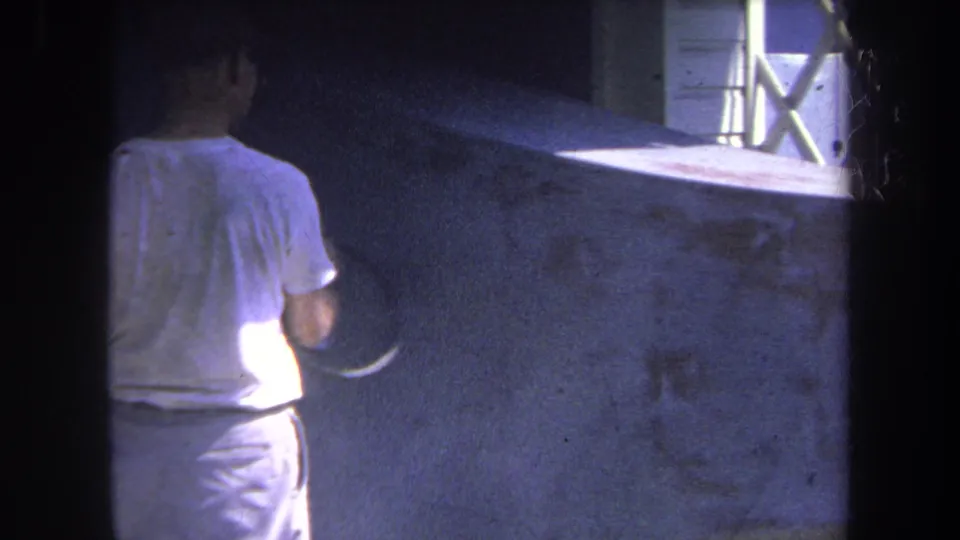 1969 Yucaipa home-movie frame showing a man from behind using spray equipment on a concrete wall.