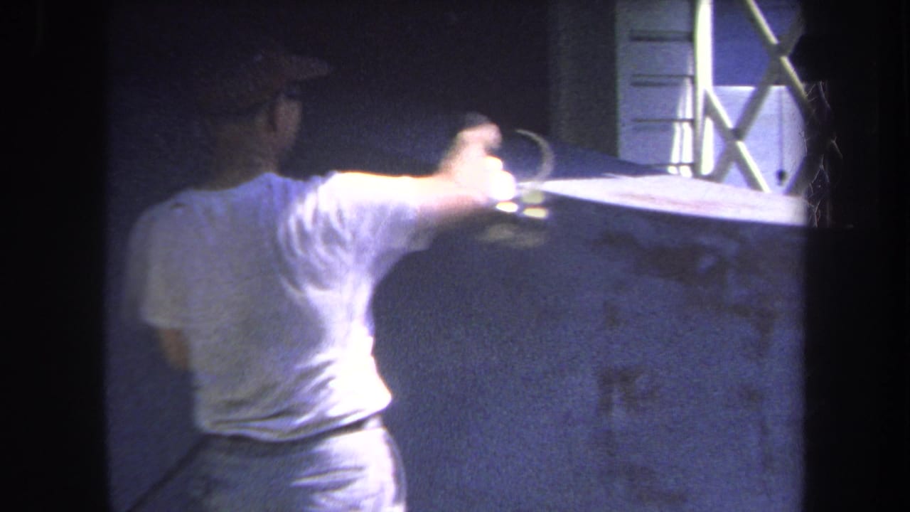 1969 Yucaipa home-movie frame showing a man in glasses and a cap using a spray gun on a concrete surface.