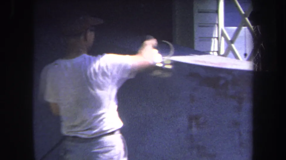 1969 Yucaipa home-movie frame showing a man in glasses and a cap using a spray gun on a concrete surface.