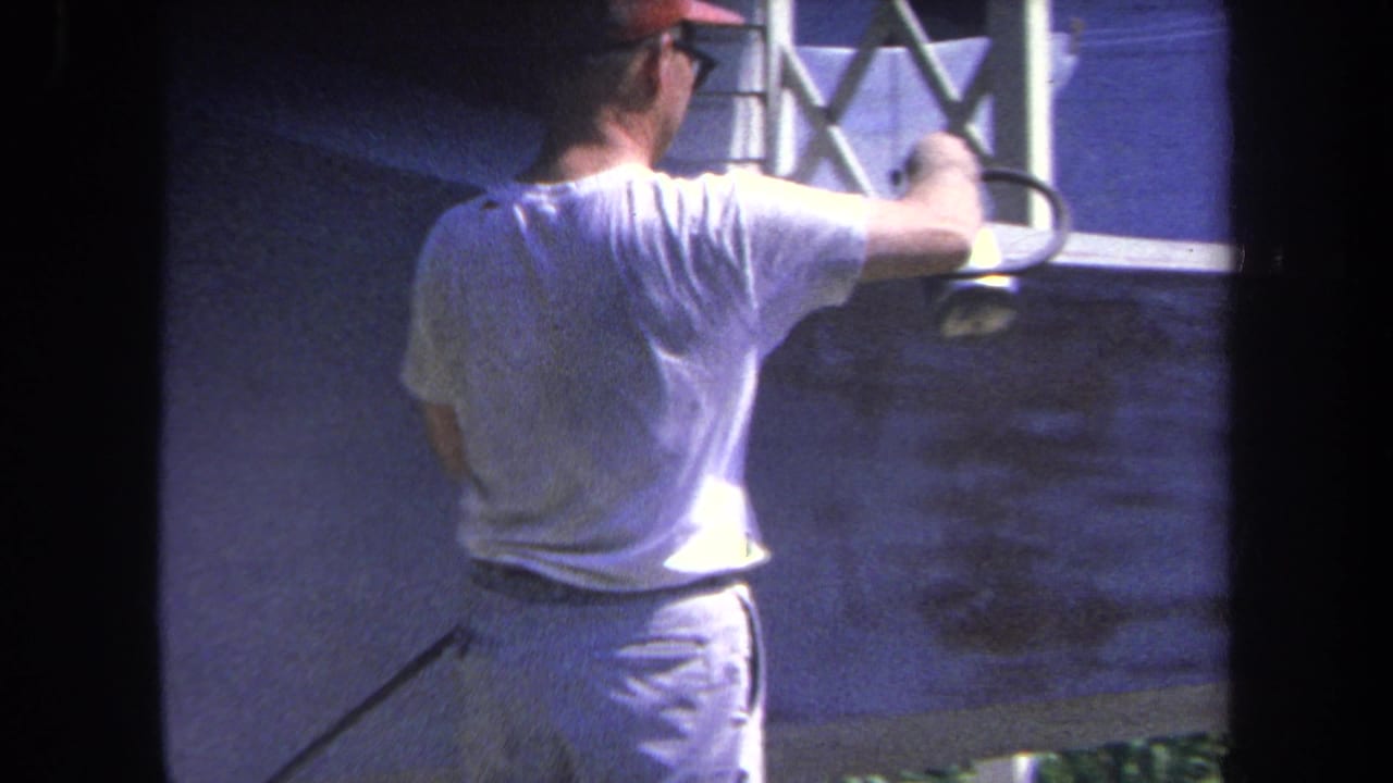 Man seen from behind spraying paint near a fence and concrete wall.