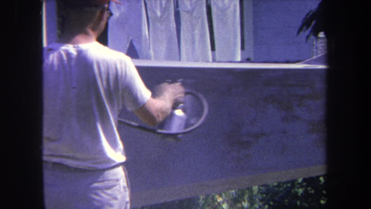 1969 Yucaipa-area 8mm frame showing a man from behind using a spray gun on a backyard wall with laundry above.