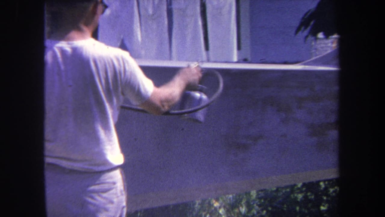 Man holds a spray gun against a wall below hanging laundry.
