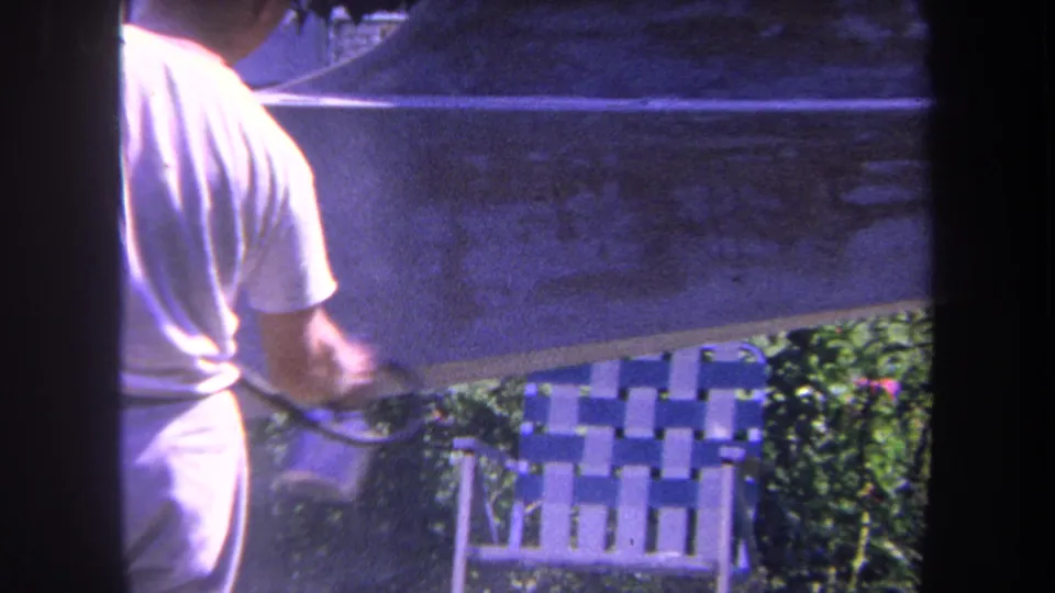 1969 Yucaipa-area home-movie frame showing a man handling a spray gun or hose while working on a large outdoor surface.