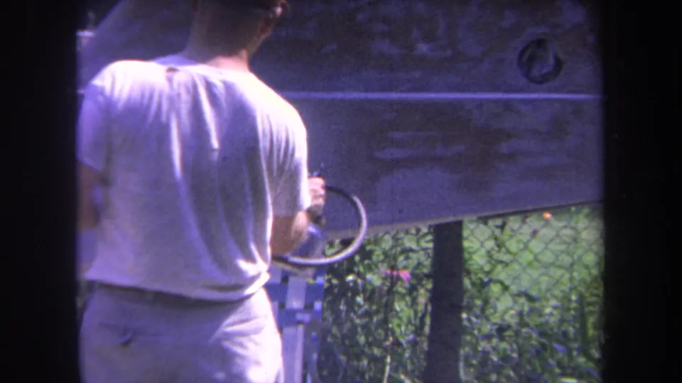 The man is visible from behind holding a looped hose near the boat side in the 1969 Yucaipa home-movie scene.