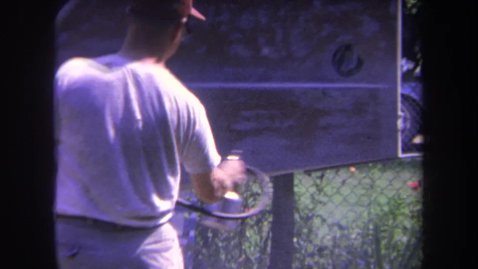 A man in a white T-shirt and red cap appears to spray paint the tail area of a small aircraft in outdoor daylight.