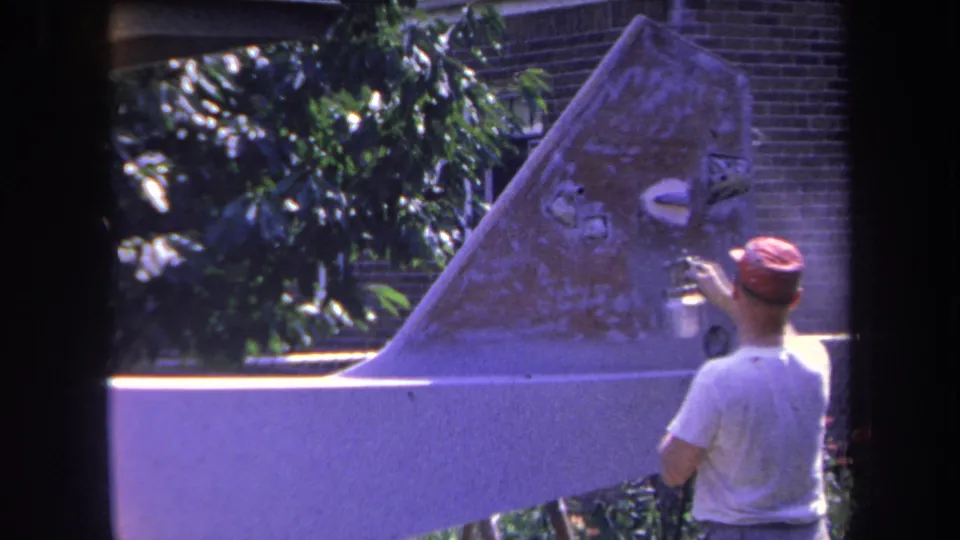 A man in a red cap stands beside the small aircraft tail in a 1969 outdoor home-movie view from Yucaipa, California.