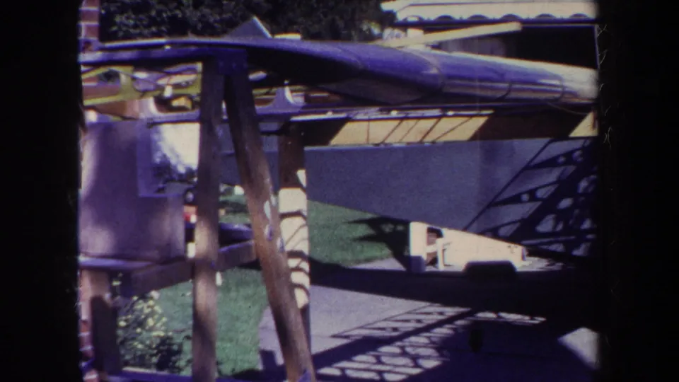 The final frame shows the aircraft tail assembly and structural frame supported outside near grass and a building.