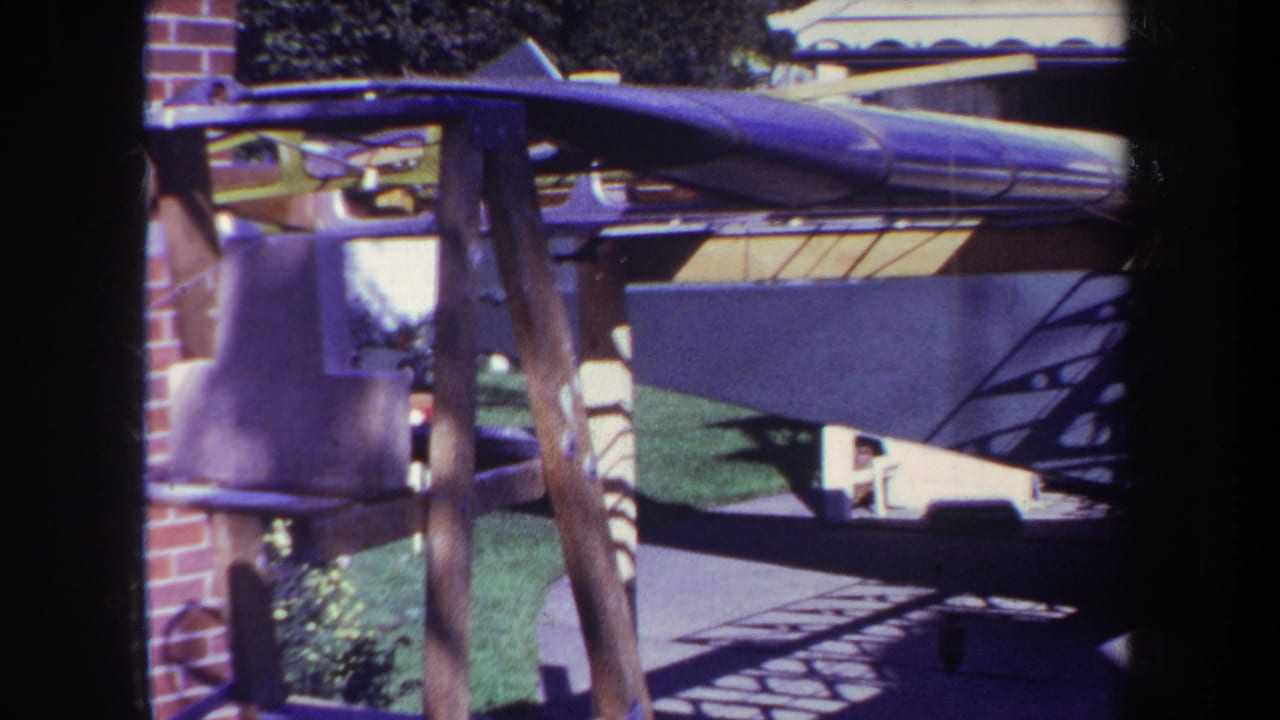 Side view of a green biplane parked near a brick wall and driveway.