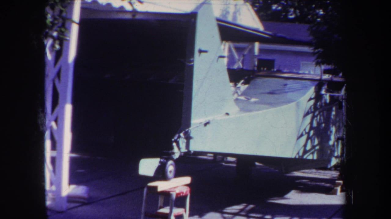White aircraft tail on a trailer in a sunny driveway beside a garage or carport.