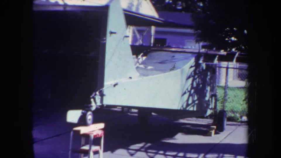 1969 Yucaipa frame with a white aircraft on a wheeled trailer, seen from a shaded residential driveway.
