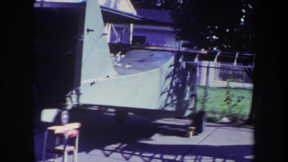 Home-movie frame from 1969 showing the aircraft trailer shifted slightly across a suburban driveway scene in Yucaipa.