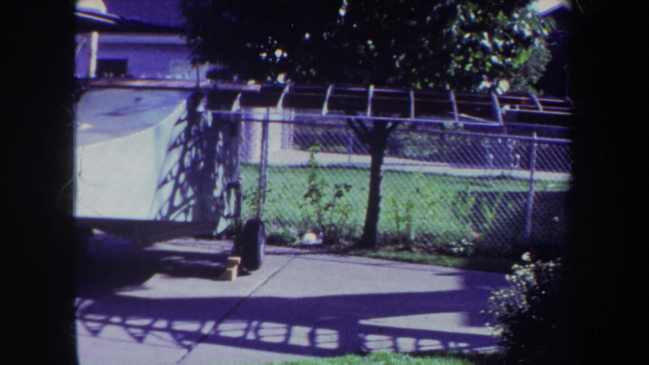Backyard patio and chain-link fence with lawn, trees, and the white structure partly visible.