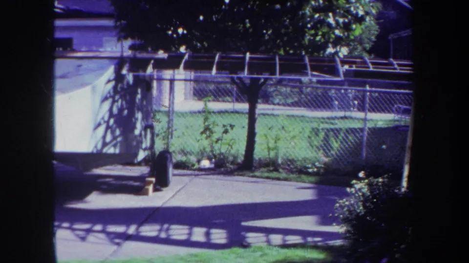 1969 Yucaipa home-movie frame showing a fenced backyard, covered pool area, lawn, patio shadows, and a white watercraft on a trailer.