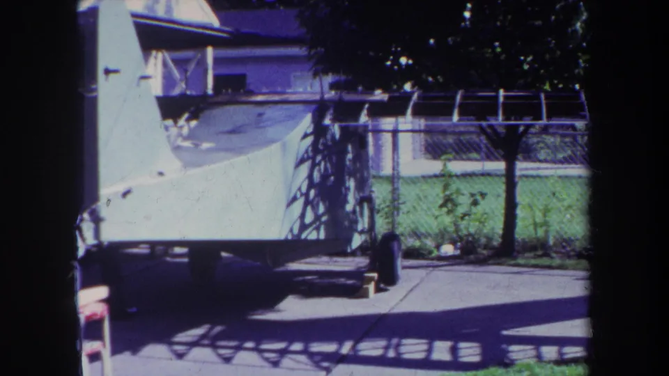 1969 Yucaipa home-movie frame centered on a white watercraft on a trailer beside a chain-link fence and covered pool area.