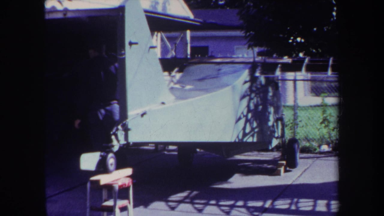 1969 Yucaipa home-movie frame showing a white boat on a trailer in a suburban backyard near house siding and shade.