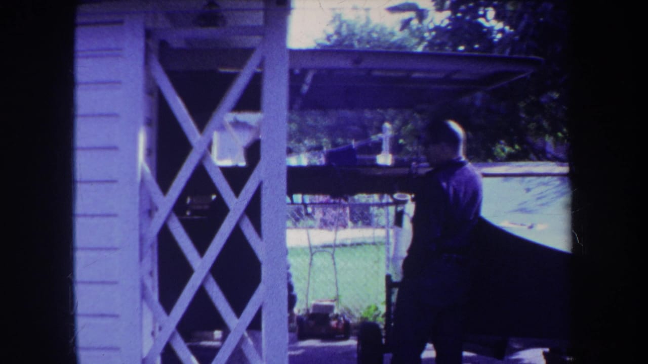Man in a dark shirt stands beside a boat near a white lattice porch.