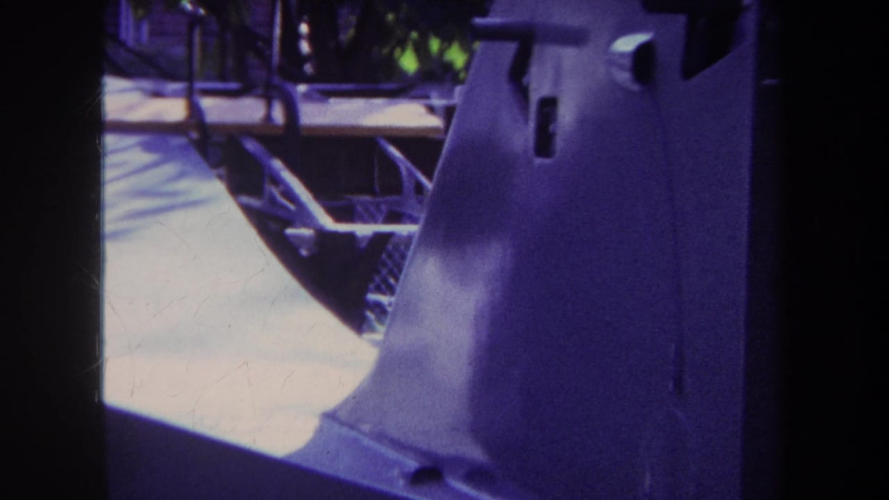 1969 Yucaipa home-movie frame with chain-link fencing, pale wood framing, steps, greenery, and heavy purple color cast.
