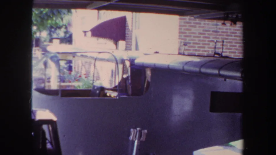 1969 8mm frame showing the home-built airplane from a fixed garage perspective in Yucaipa, with brickwork and an awning outside.