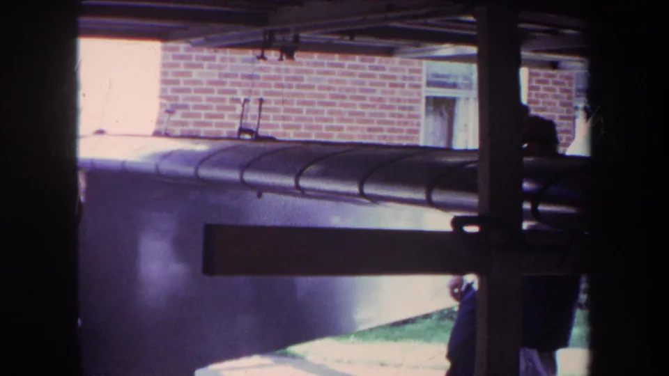 1969 Volmer Yucaipa frame with the model airplane foregrounded under a covered structure and a partially visible person near the right side.